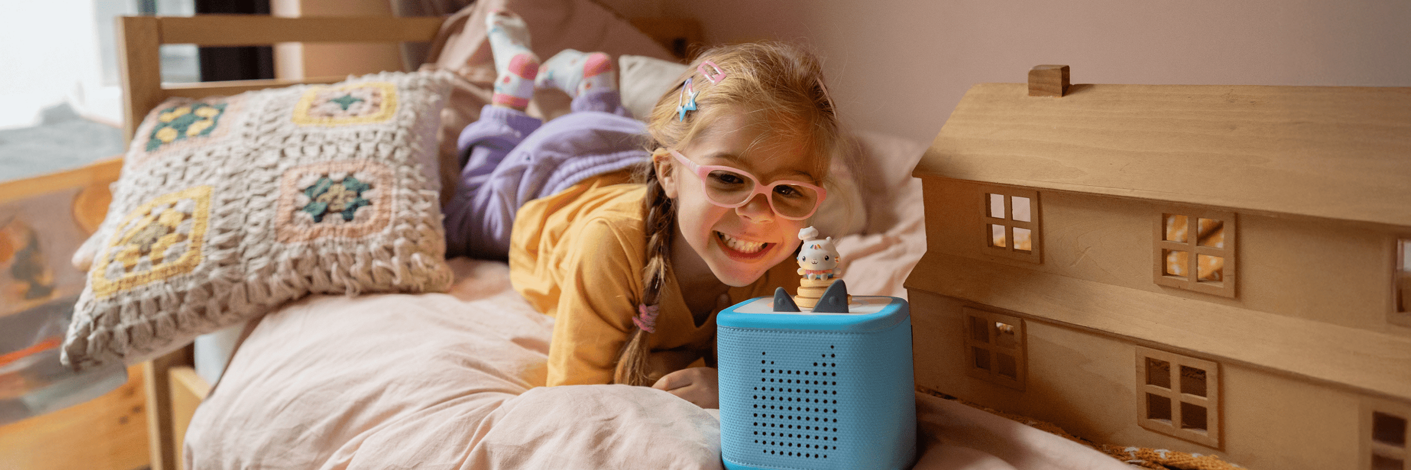 Child playing with a toy house and blue toniebox on a bed